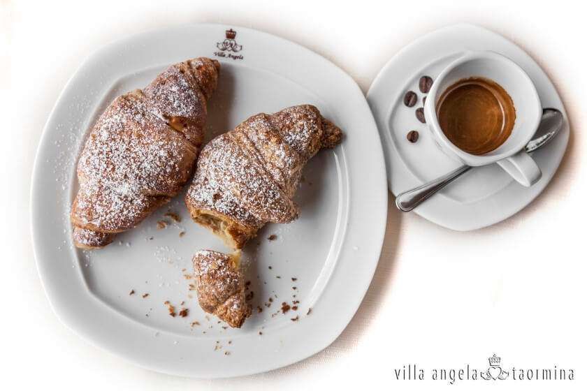 Two croissants on a white plate next to a cup of coffee