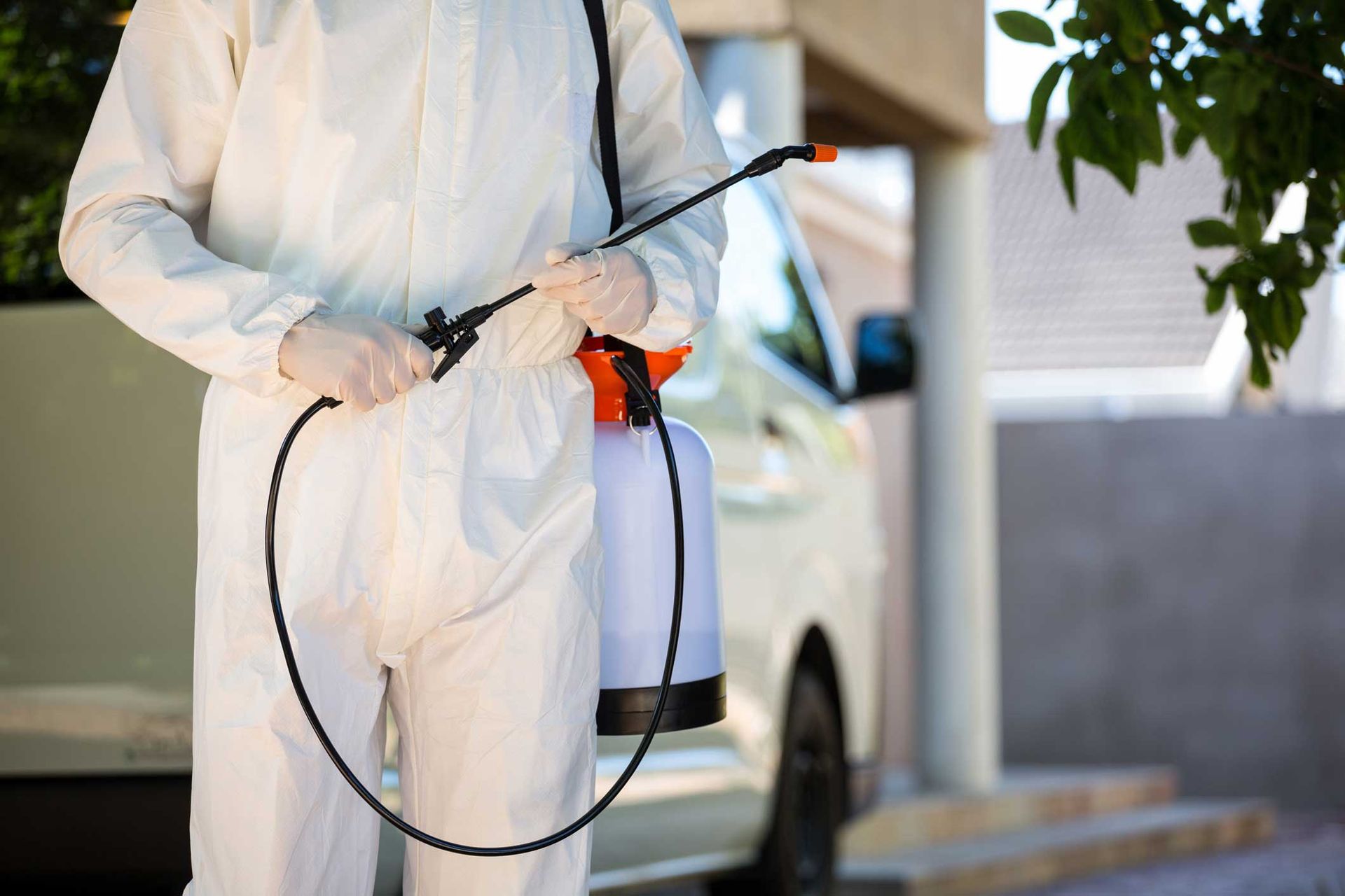 Person in white protective suit spraying a vehicle outdoors with a handheld sprayer
