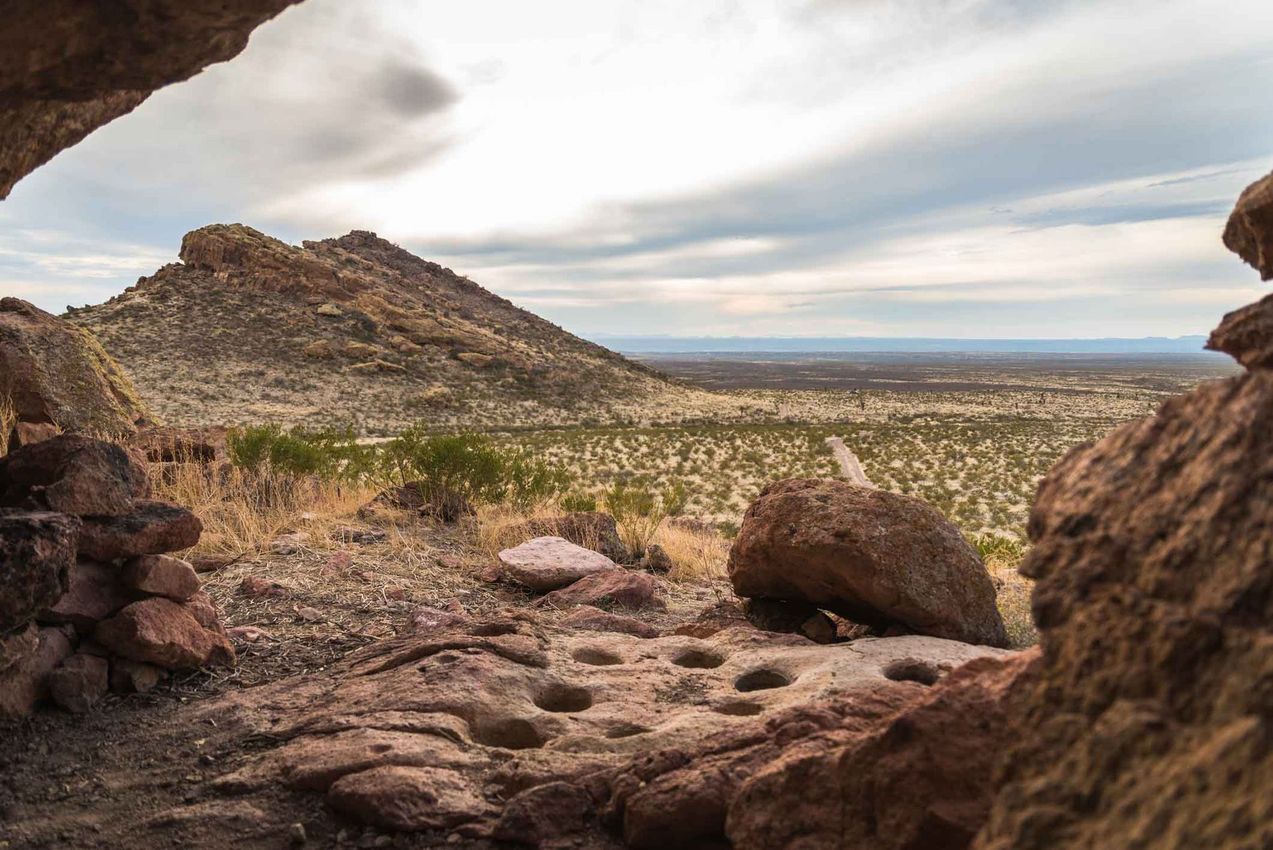 Rocky desert landscape viewed from a shaded cave opening under a cloudy sky