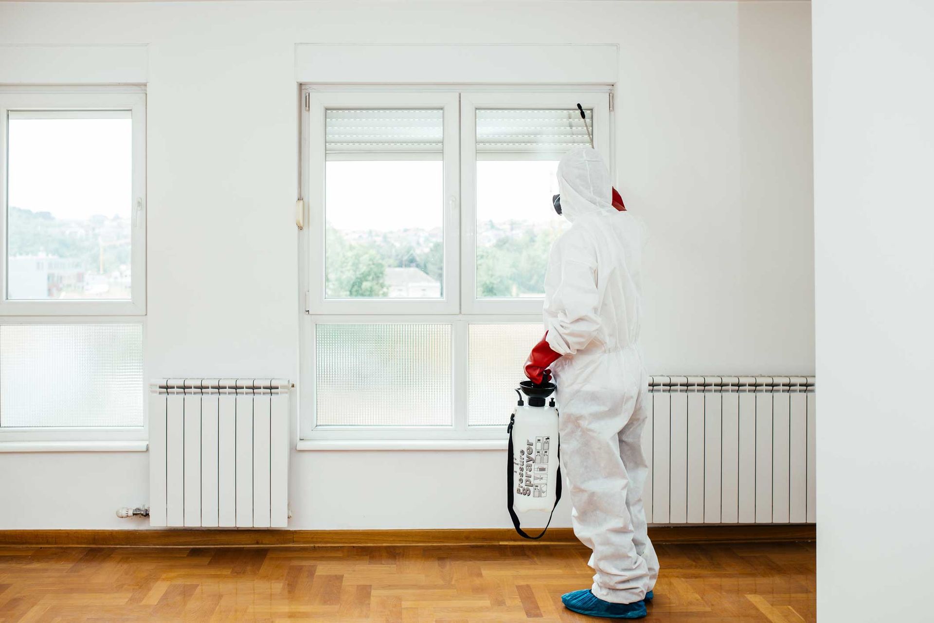 Person in white protective suit spraying disinfectant in a bright empty room