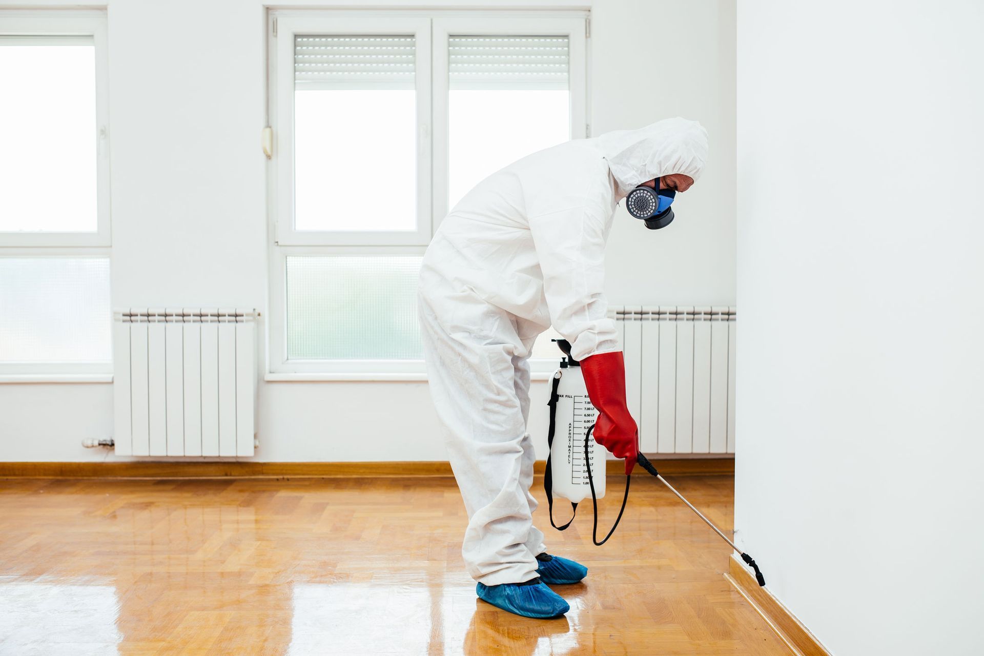 Worker in white protective suit using a floor sander in a bright empty room