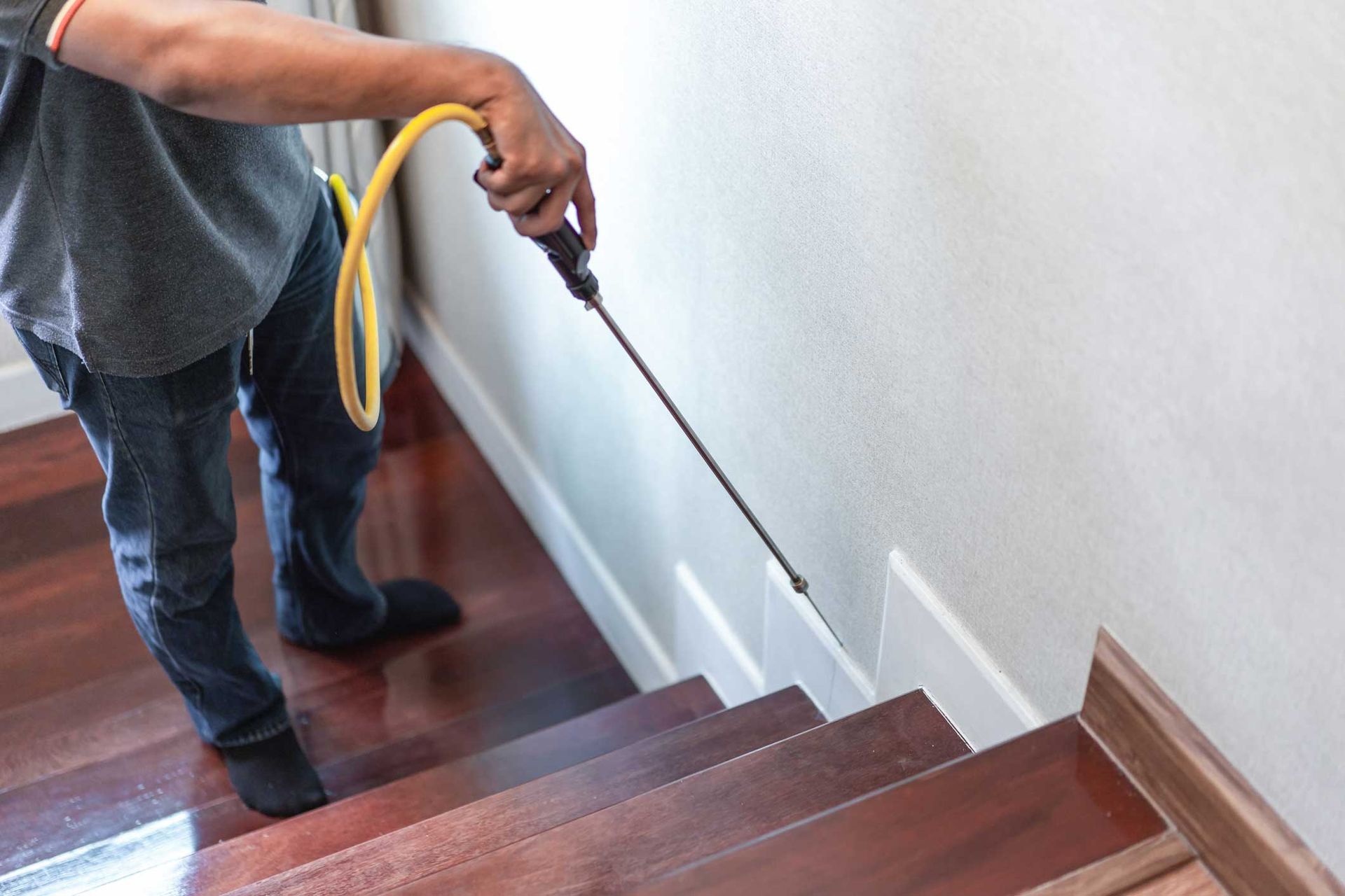 Person spraying a staircase railing with a cleaning hose in a home interior