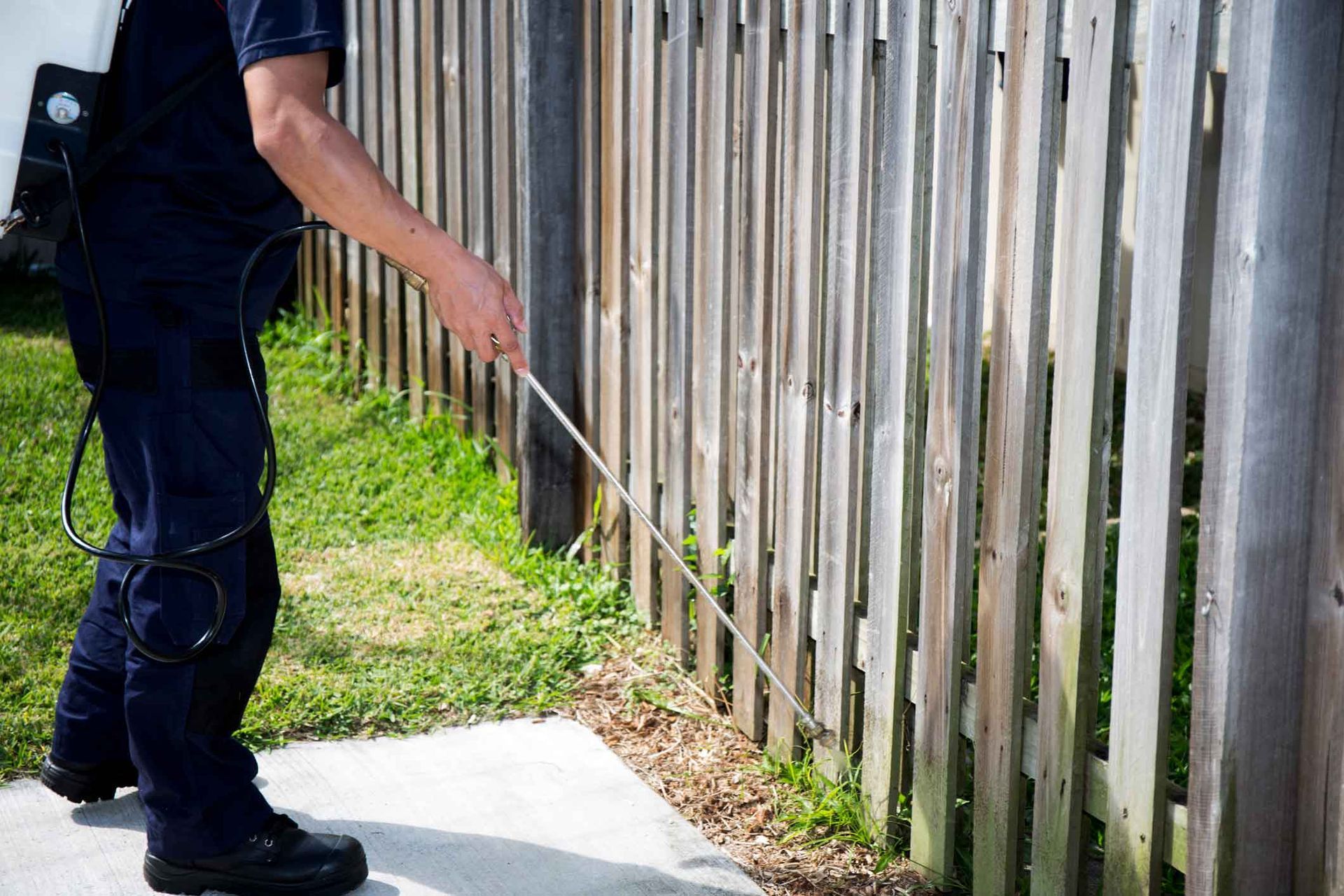 Person using a long pole to measure along a wooden fence beside a sidewalk.