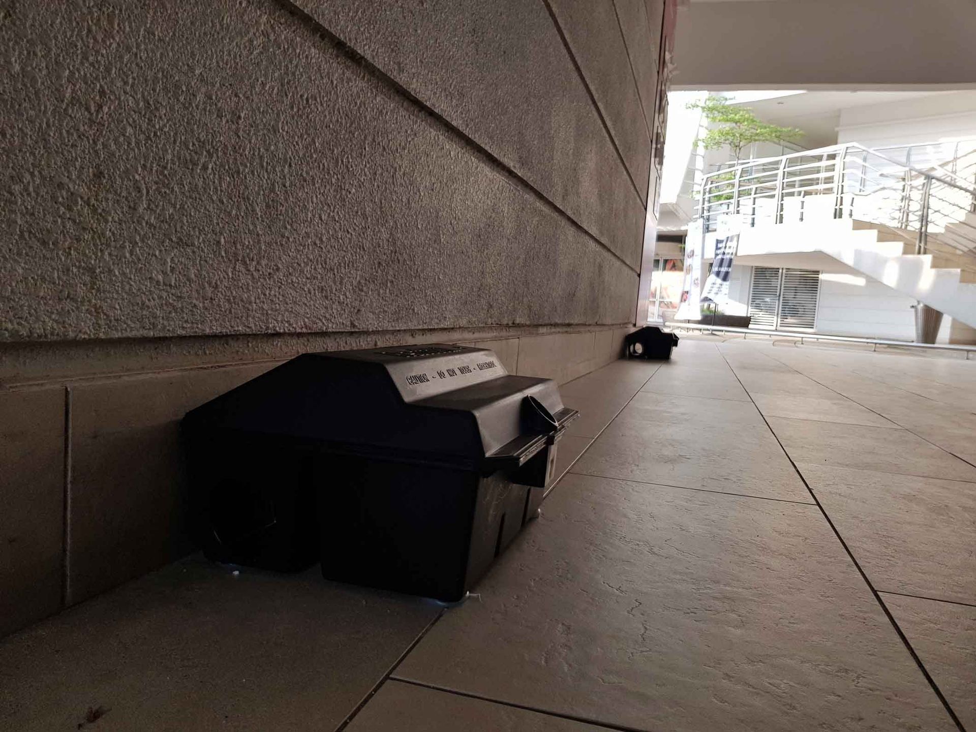 Black box on a sidewalk beside a concrete wall, near a stairway outdoors