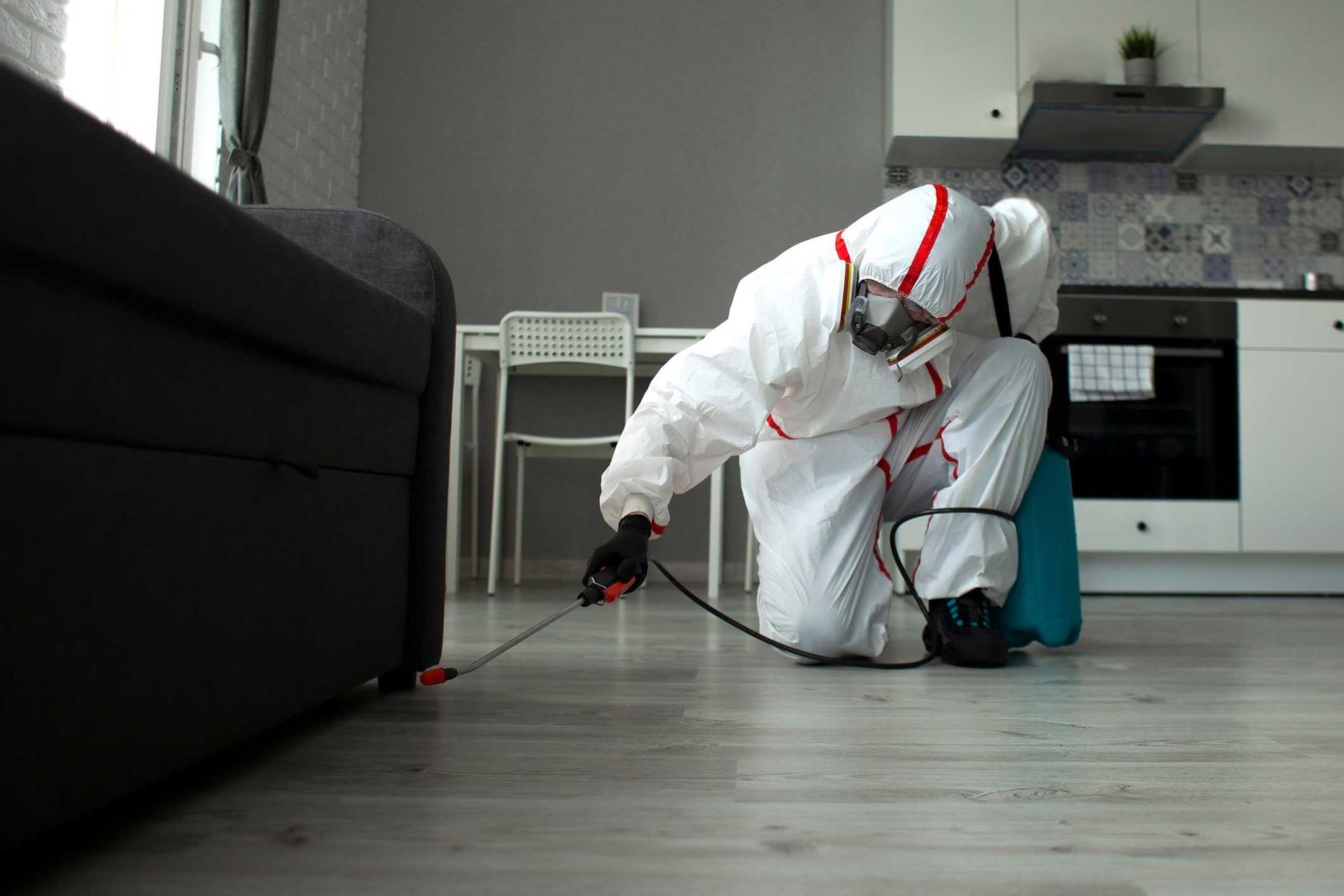 Person in white protective suit cleaning a kitchen floor with a spray bottle and cloth.