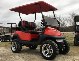A red golf cart is parked in a dirt field.