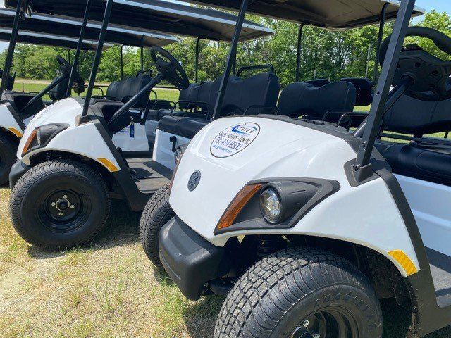 Three white golf carts are parked next to each other on a grassy field.