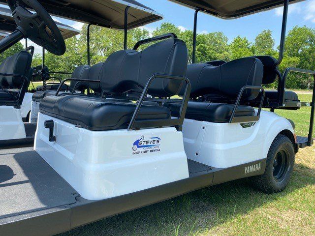 A white golf cart with black seats is parked on a grassy field.