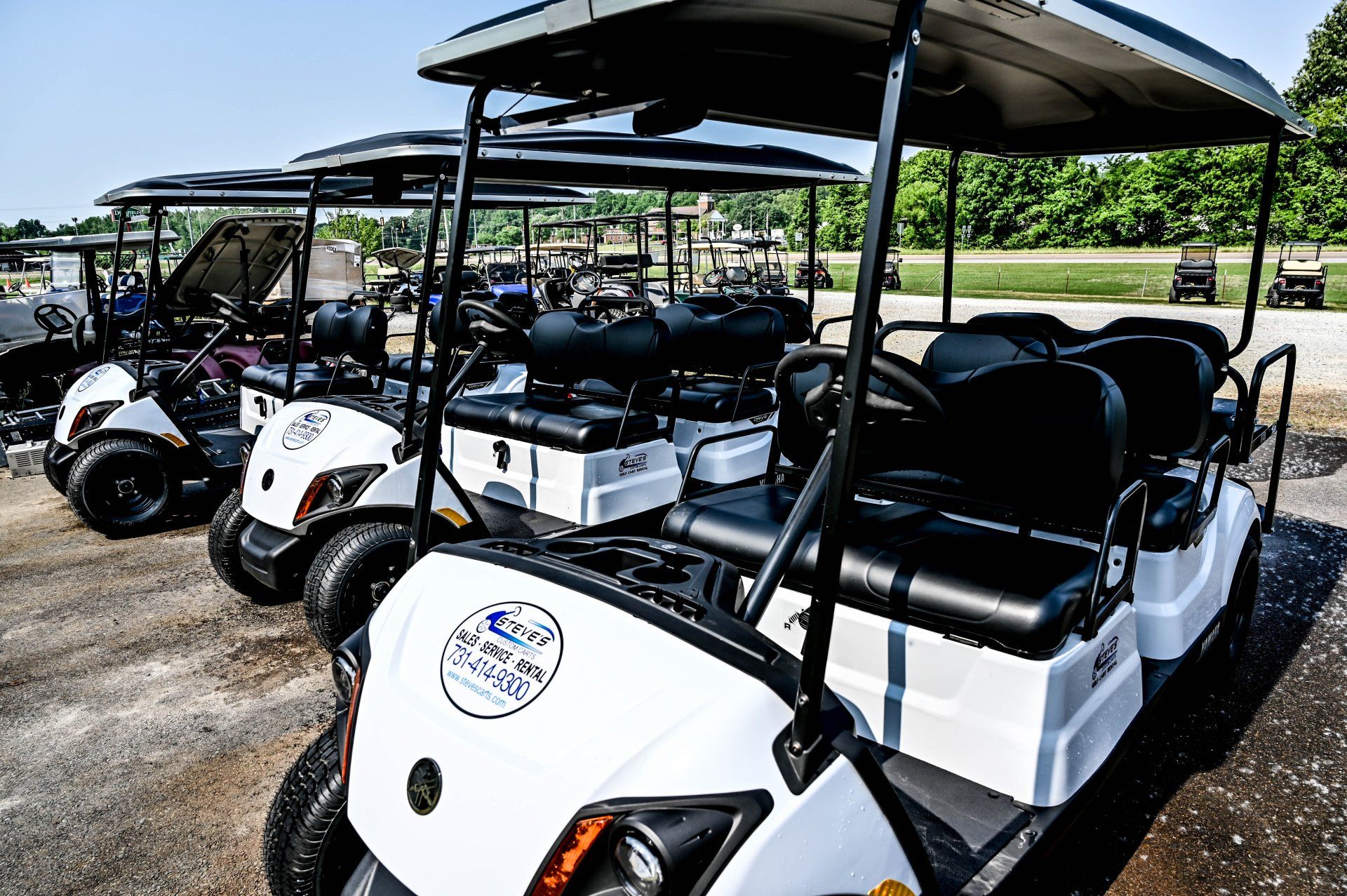 A row of white golf carts are parked in a parking lot.