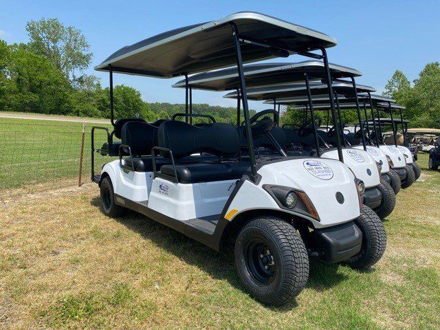 A row of white golf carts are parked in a grassy field.