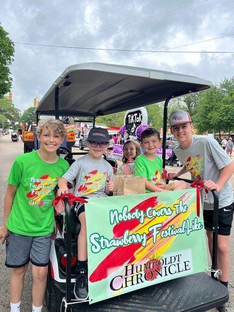 A group of kids are riding in a golf cart with a sign that says strawberry festival