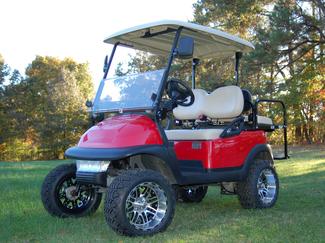 A red golf cart is parked on a lush green field.