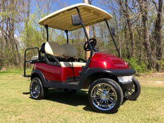 A red golf cart is parked on a lush green field.