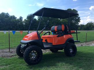 An orange golf cart is parked in a grassy field.
