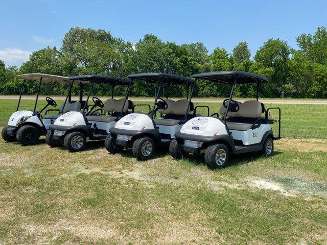 A row of golf carts are parked in a grassy field.
