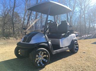 A white and black golf cart is parked in a dirt field.