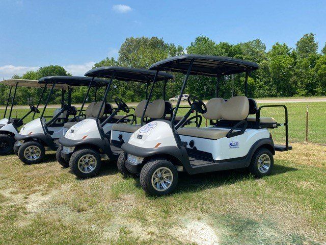 A row of golf carts are parked in a grassy field.