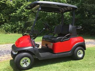A red golf cart is parked on a lush green field.
