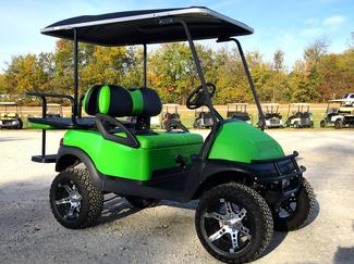 A green and black golf cart is parked in a parking lot.