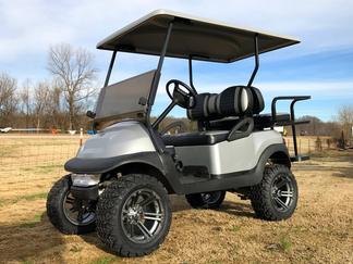 A silver golf cart is parked in a grassy field.