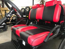 A red and black golf cart seat with a steering wheel in a garage.