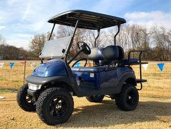 A blue golf cart is parked in a grassy field.