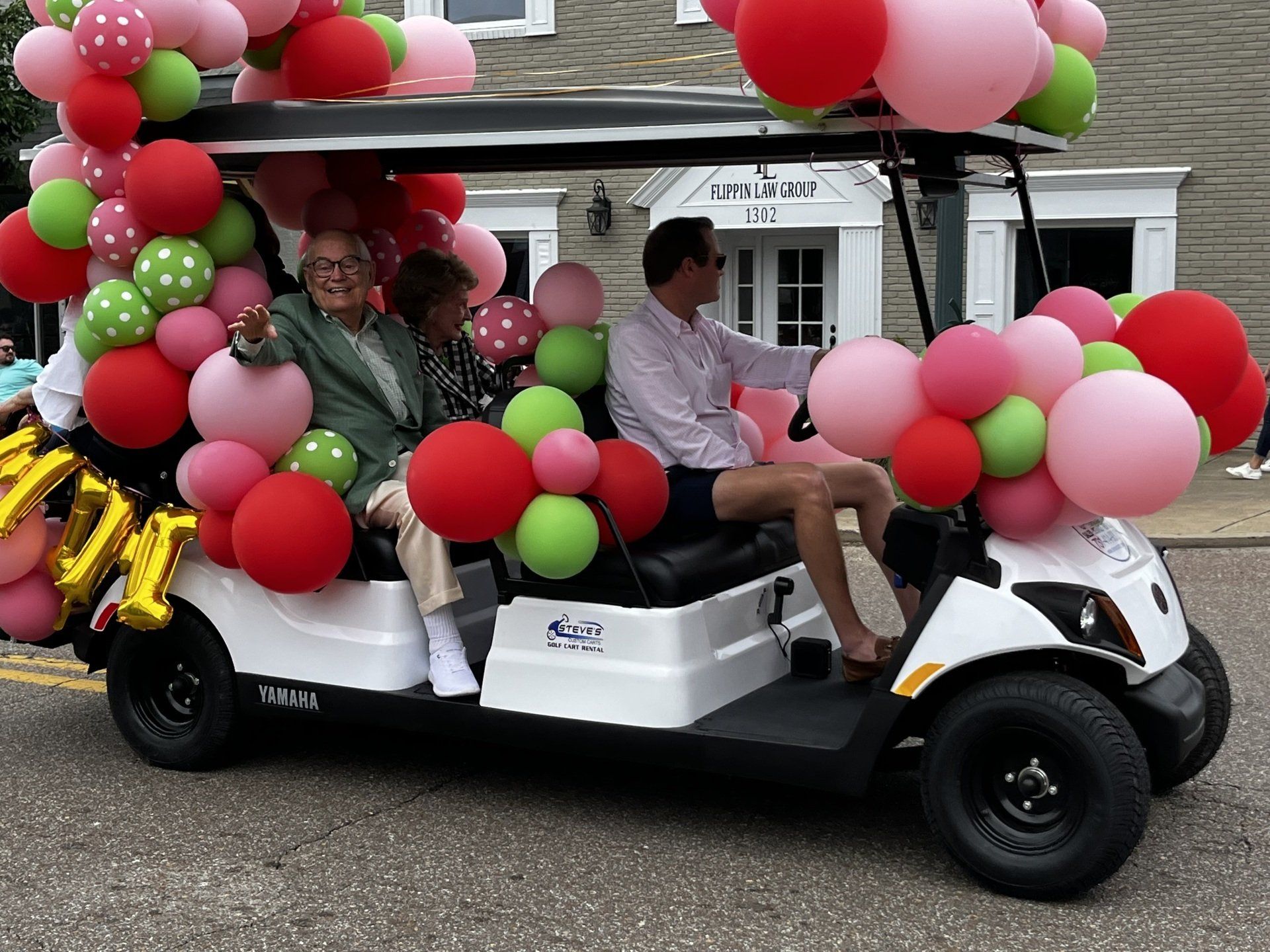 A golf cart is decorated with pink green and red balloons