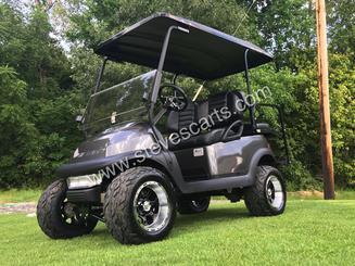 A black golf cart is parked on a lush green field.