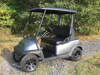 A gray golf cart is parked on a gravel road.