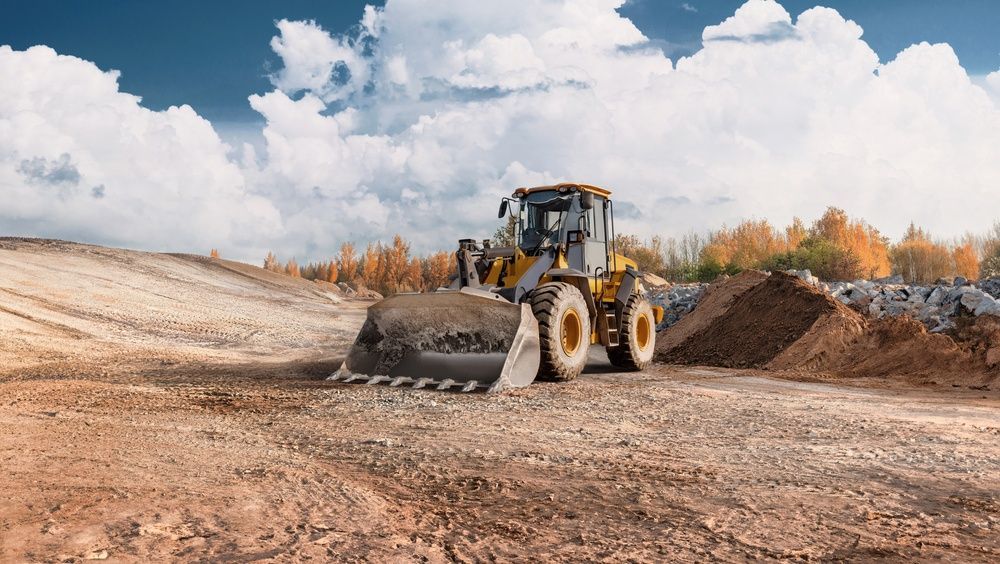 Bulldozer grading a dirt road at a construction site under a cloudy sky