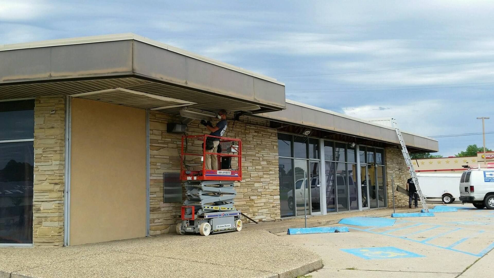 Storefront under renovation with lift, stone facade, glass windows, and a white van parked outside.