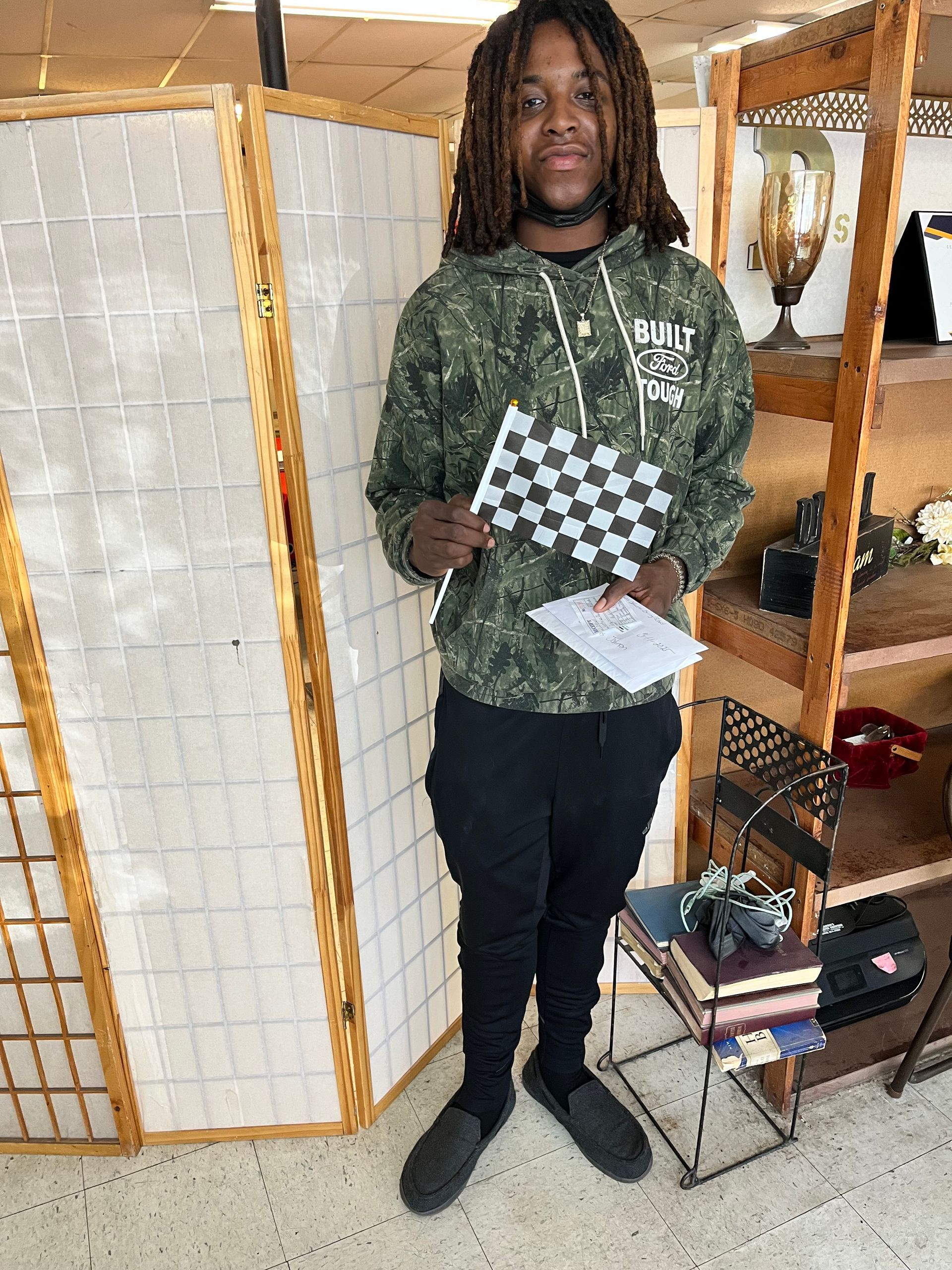 Person in camouflage hoodie holds checkered flag, standing by a folding screen.