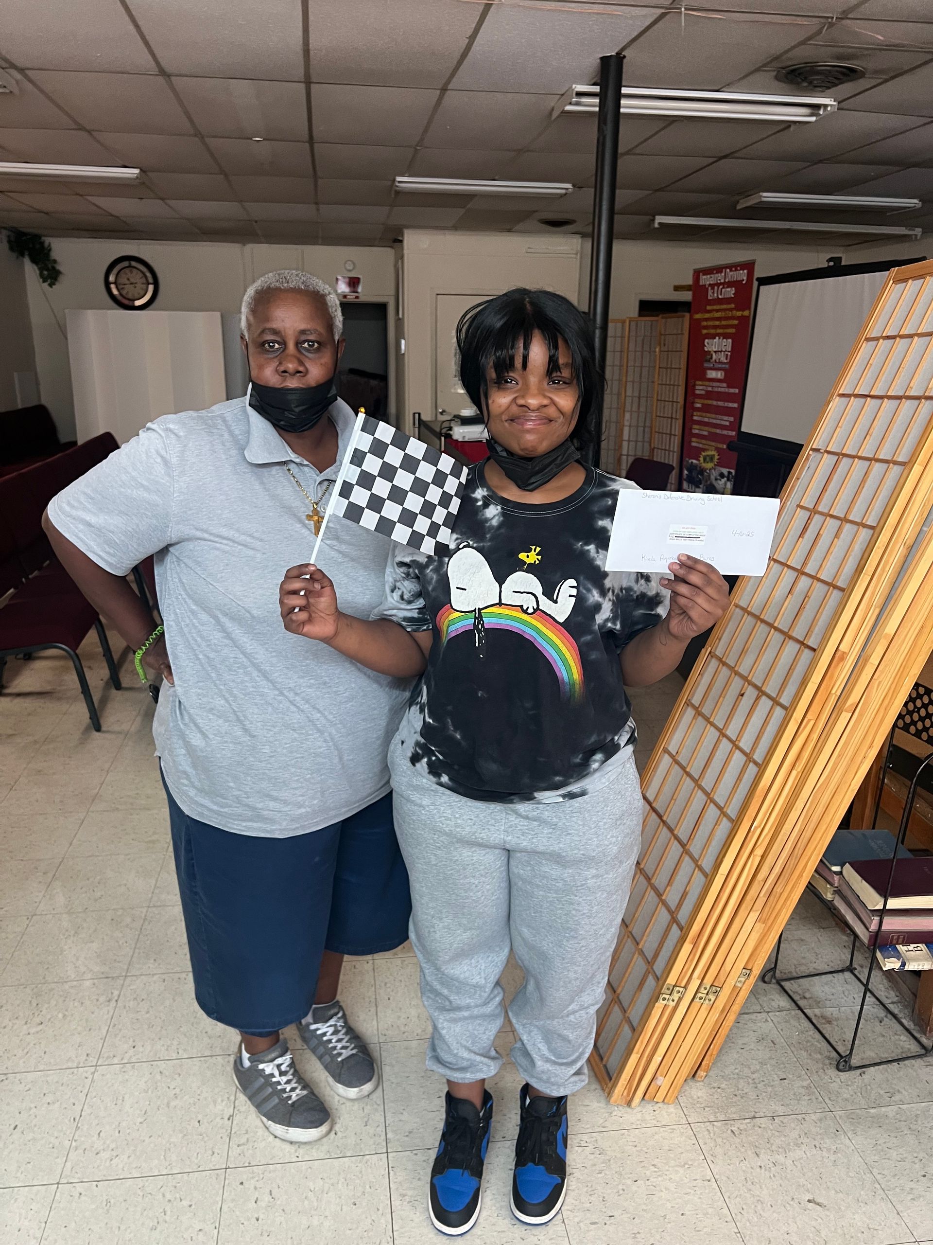 Woman holding check and checkered flag, posing with another woman indoors.