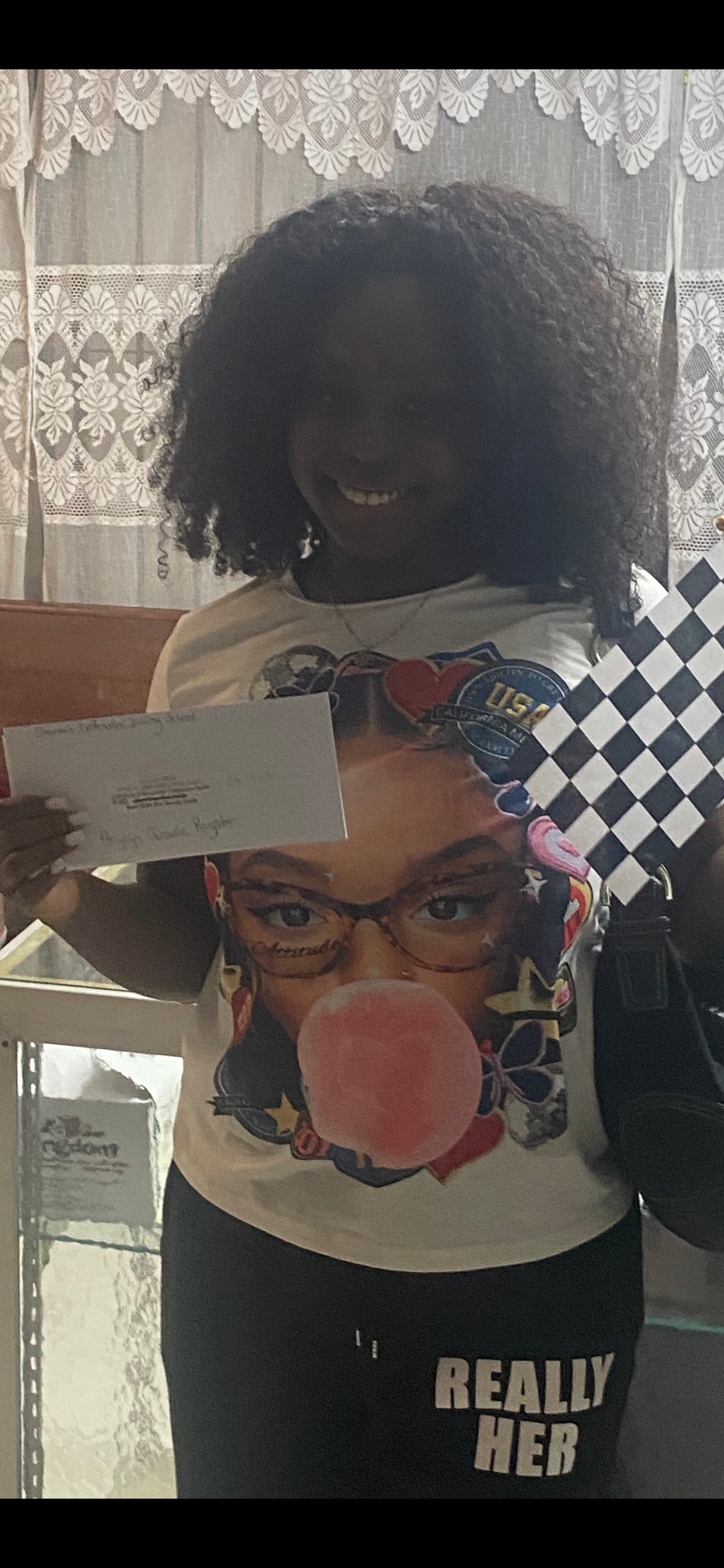 Person holding a checkered flag and a piece of paper, smiling, wearing a shirt with a face graphic