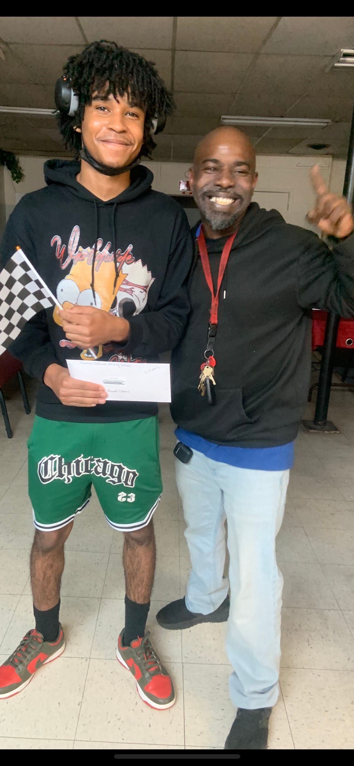 Two people, one holding a trophy and a check, posing for a photo. The other person is raising a finger.