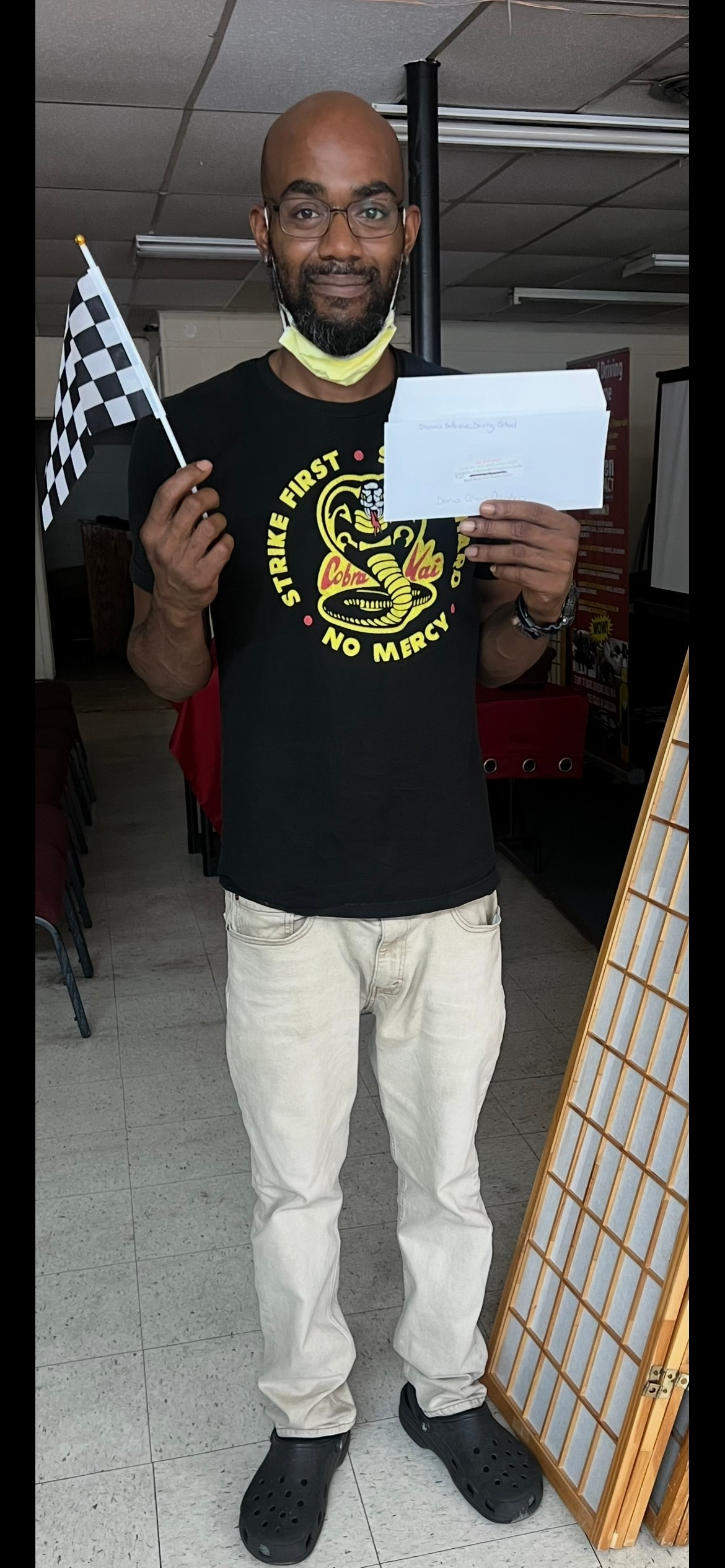 A man with a bald head, glasses, and a black shirt holding a checkered flag and a paper.