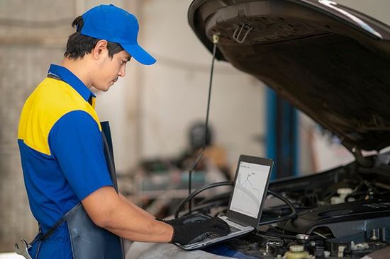 A man is working on a car with a laptop.