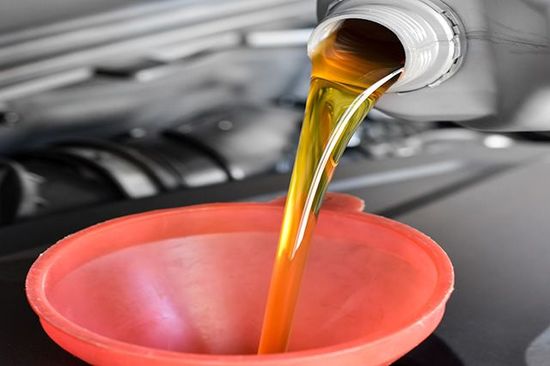 A bottle of oil is being poured into a pink bowl.