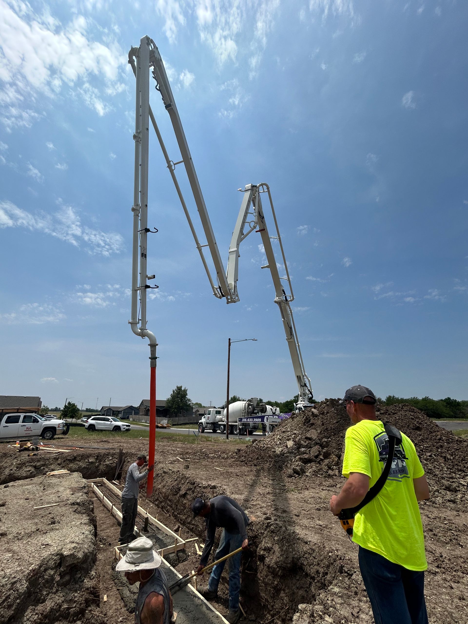 A man in a neon yellow shirt is standing in front of a concrete pump.