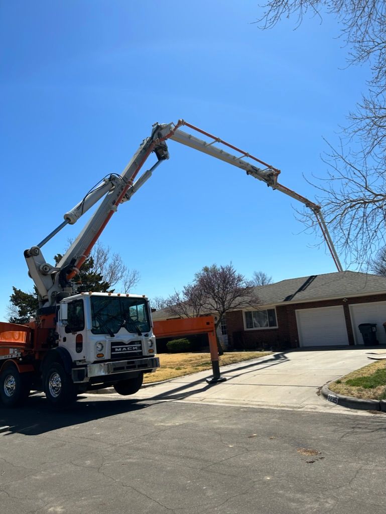 A concrete pump truck is pumping concrete into a driveway in front of a house.
