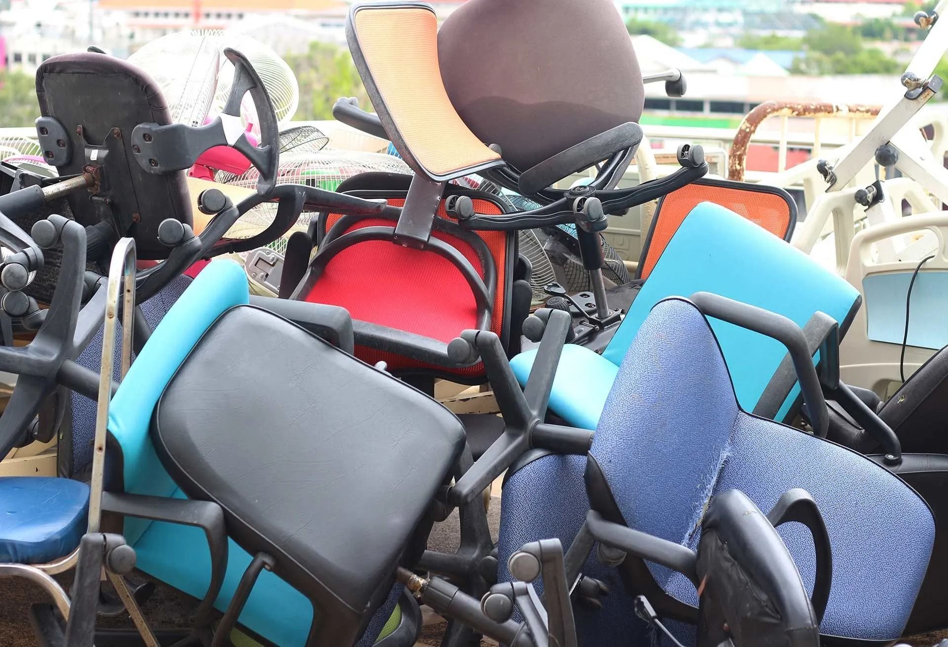 Pile of assorted folded wheelchairs in red, blue, black, and beige outdoors.