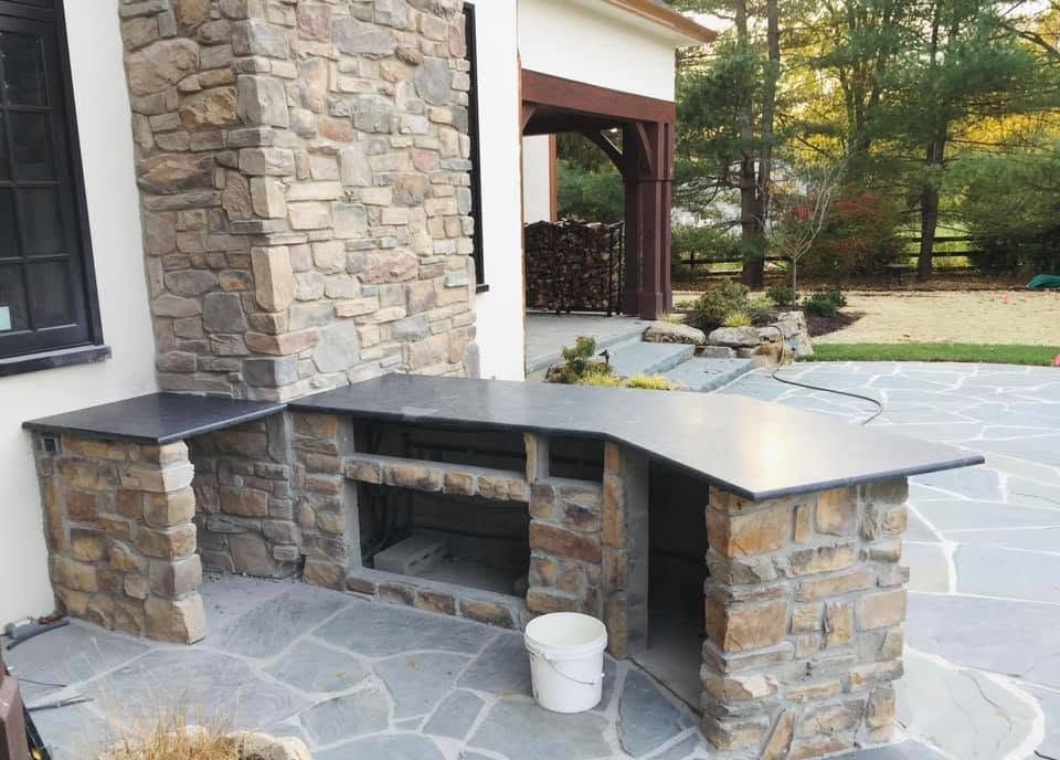 Stone outdoor fireplace and built-in bench on a patio beside a house.