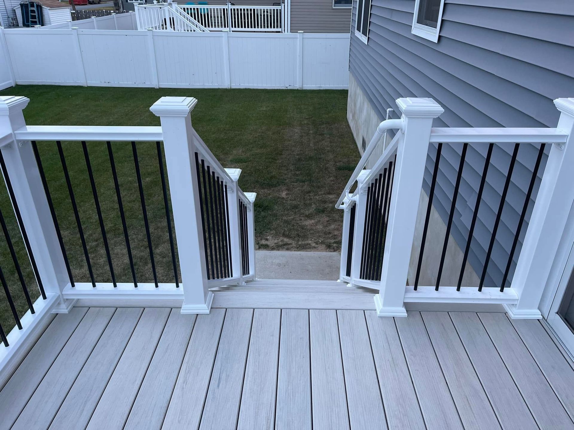 Back deck with white railing and stairs leading down to a grassy yard and white fence