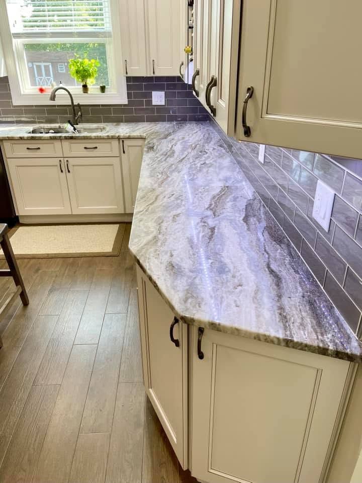 Kitchen with cream cabinets and a dramatic gray-purple marble countertop by a window and sink.