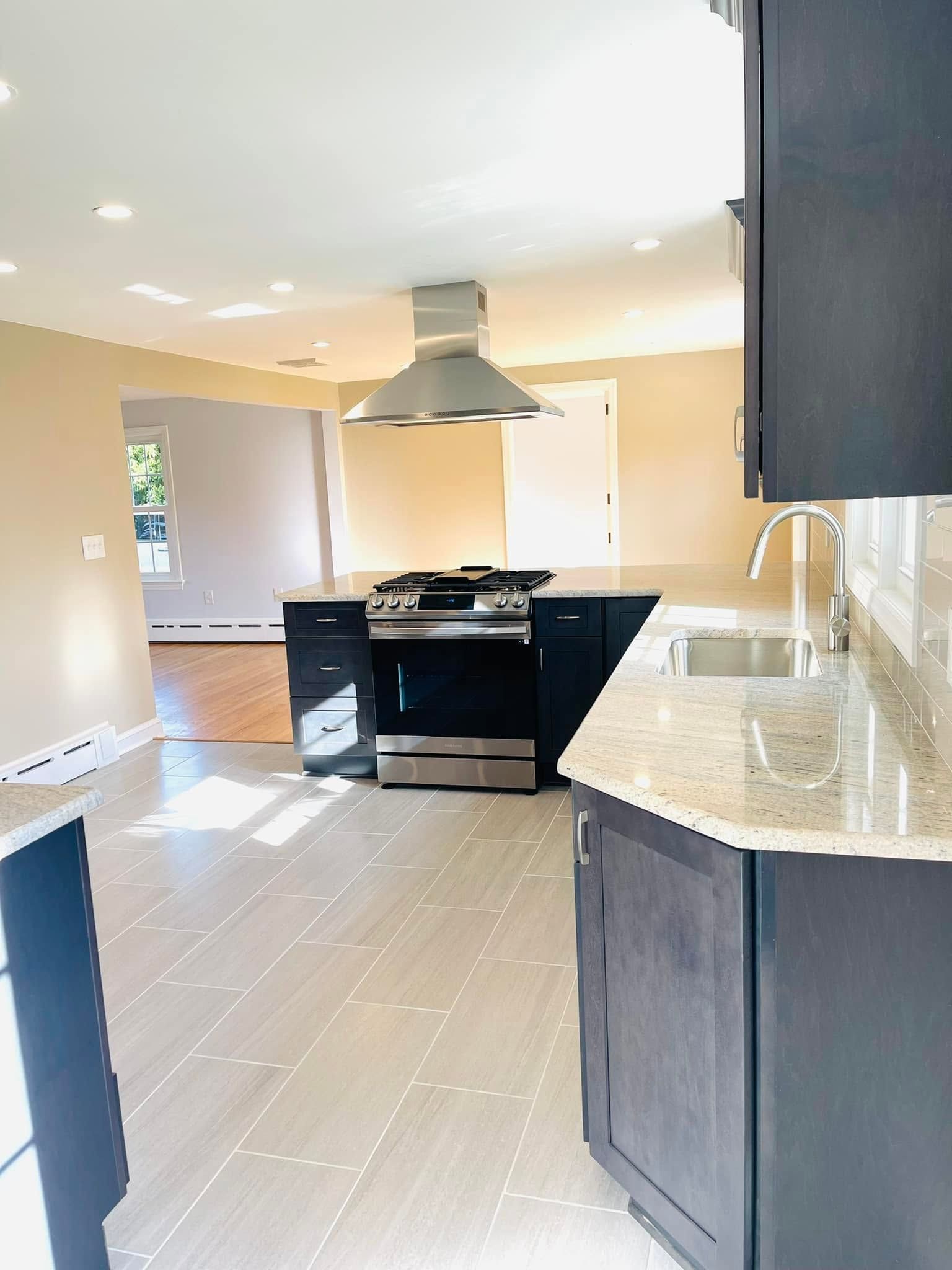 Bright empty kitchen with black stove, dark cabinets, granite countertops, and tiled floor