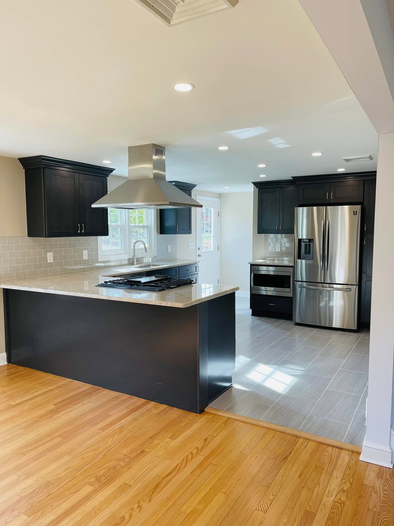 Modern kitchen with black cabinets, stainless steel appliances, and wood and tile flooring.