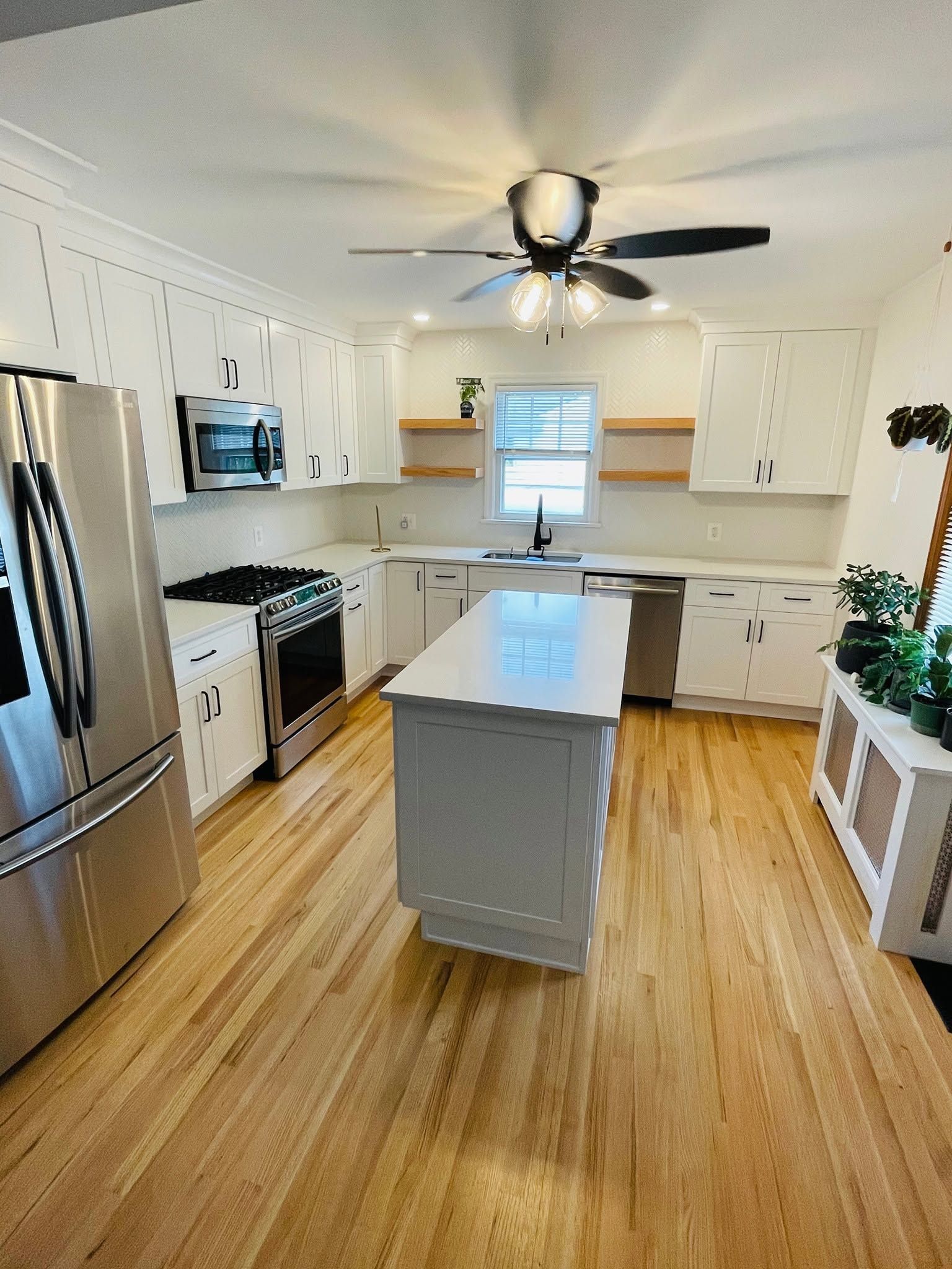 Bright white kitchen with stainless appliances, island, ceiling fan, and wood floors.