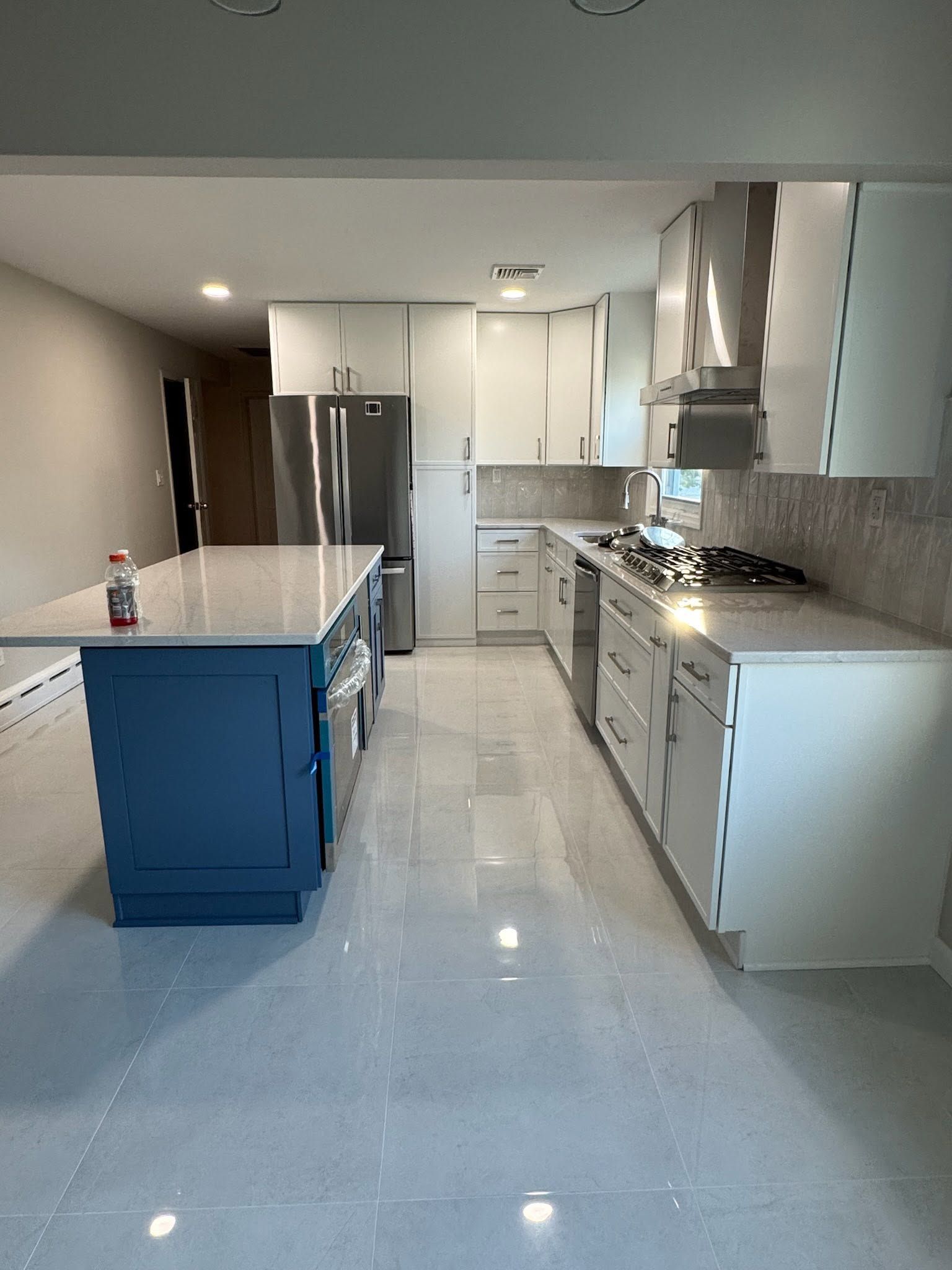 Modern kitchen with blue island, white cabinets, stainless appliances, and glossy tile floor