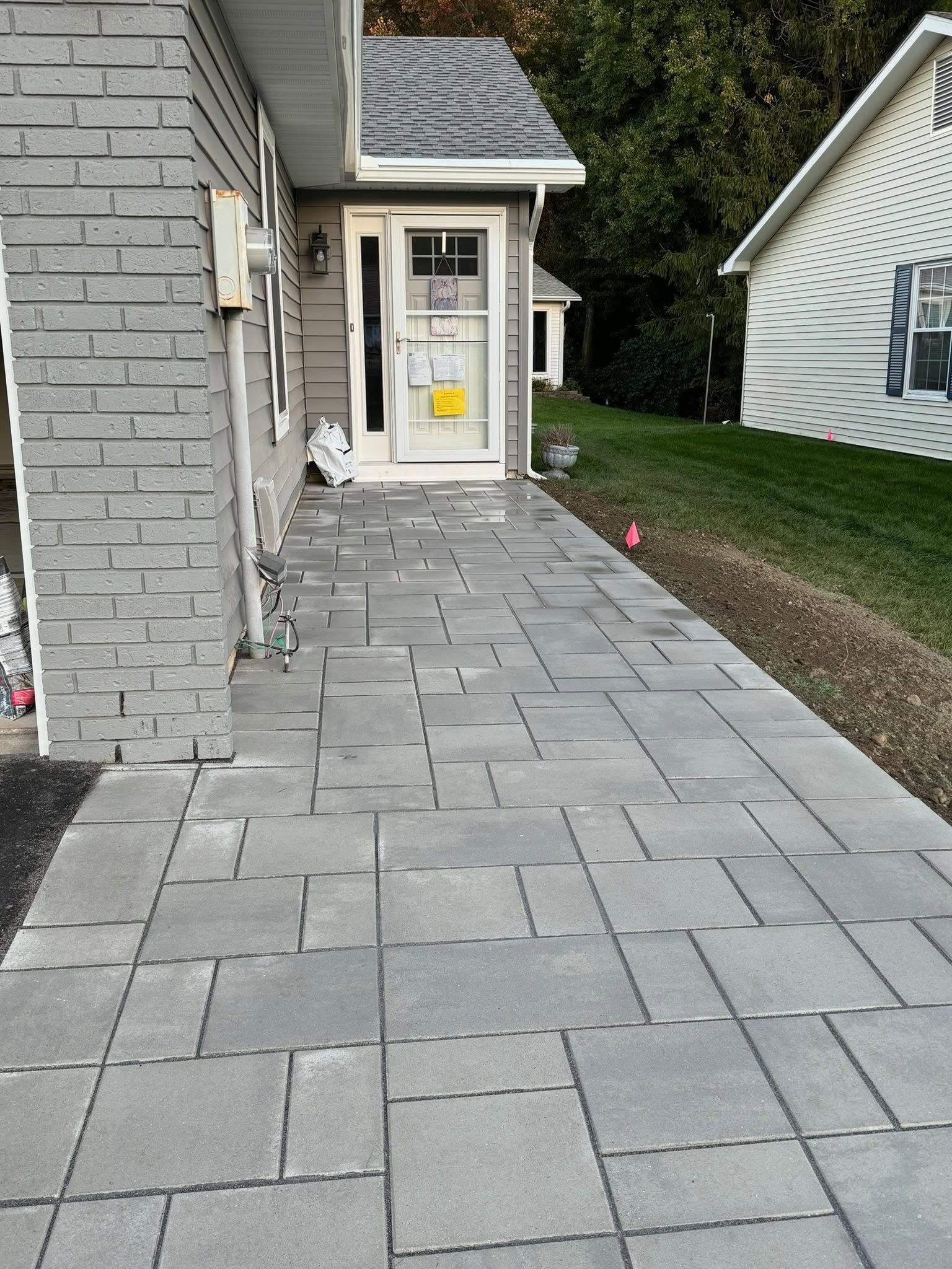 Gray stone walkway leading to a front door beside a house, with a grassy yard on the right.