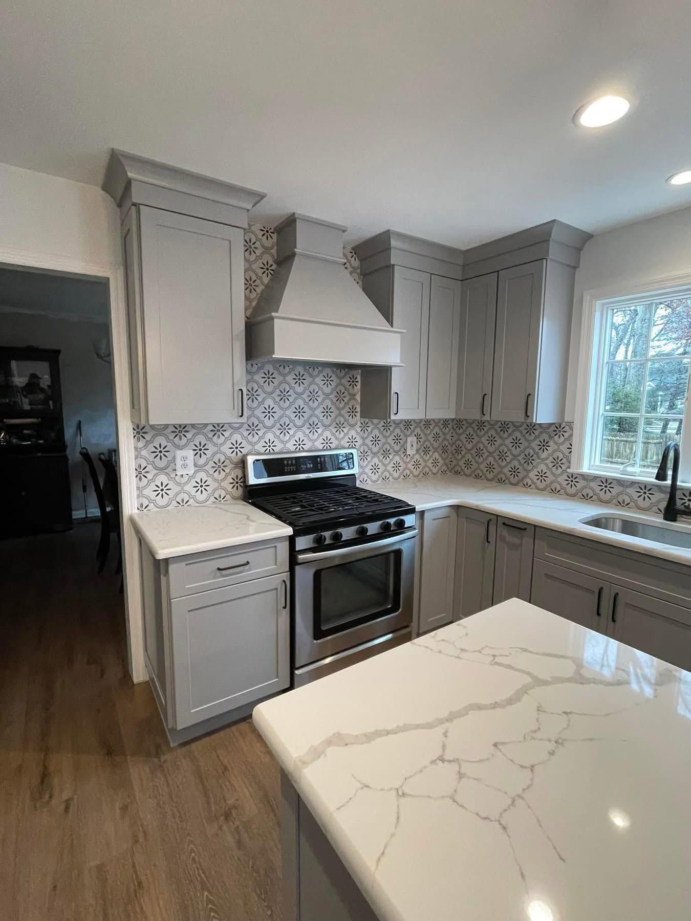 Bright modern kitchen with gray cabinets, patterned backsplash, stainless stove, and white marble island countertop